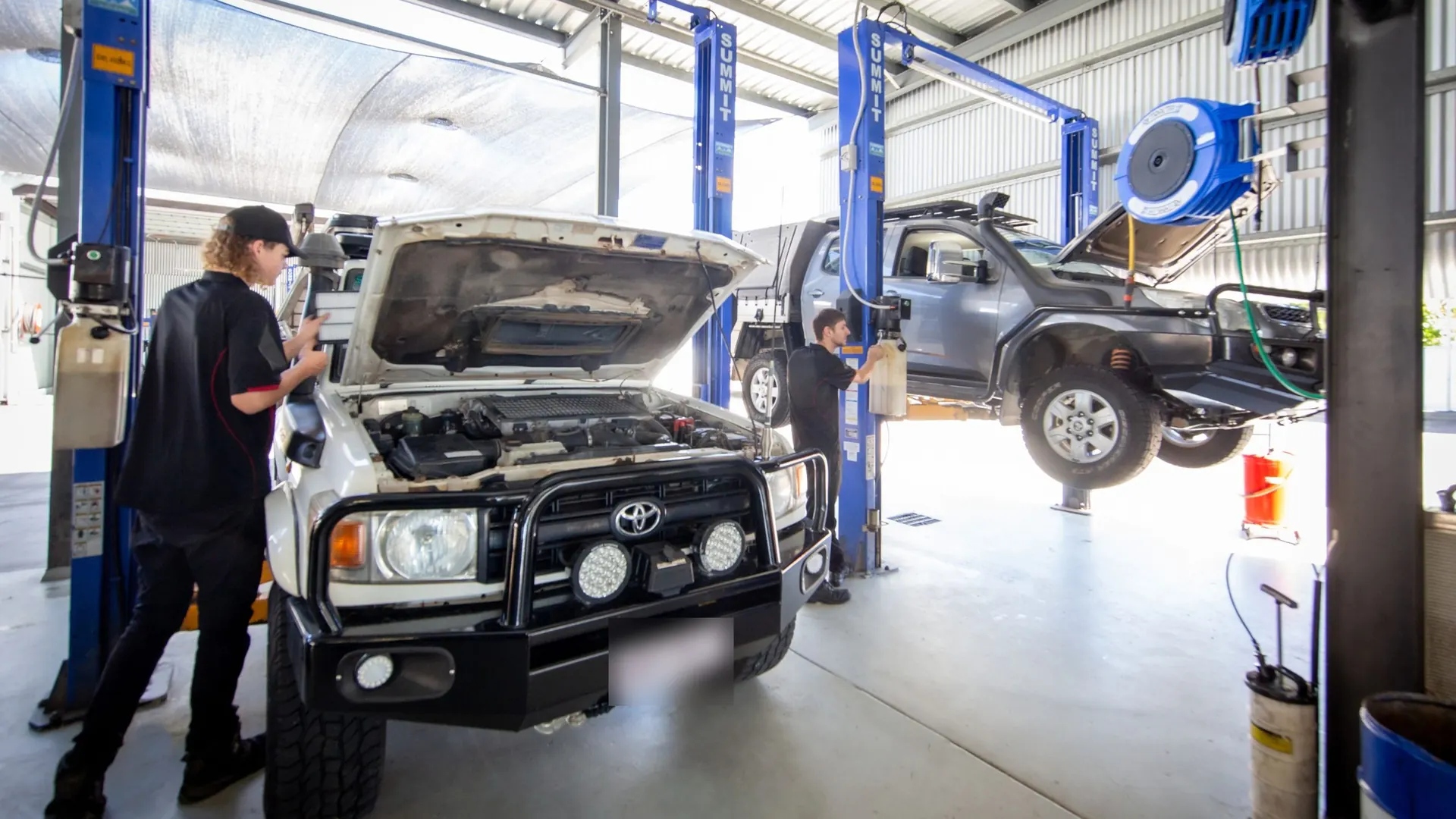A Toyota LandCruiser with bull bar and spotlights, bonnet up, in the Everything Automotive workshop in Woree, a lifted 4WD ute on the hoist behind