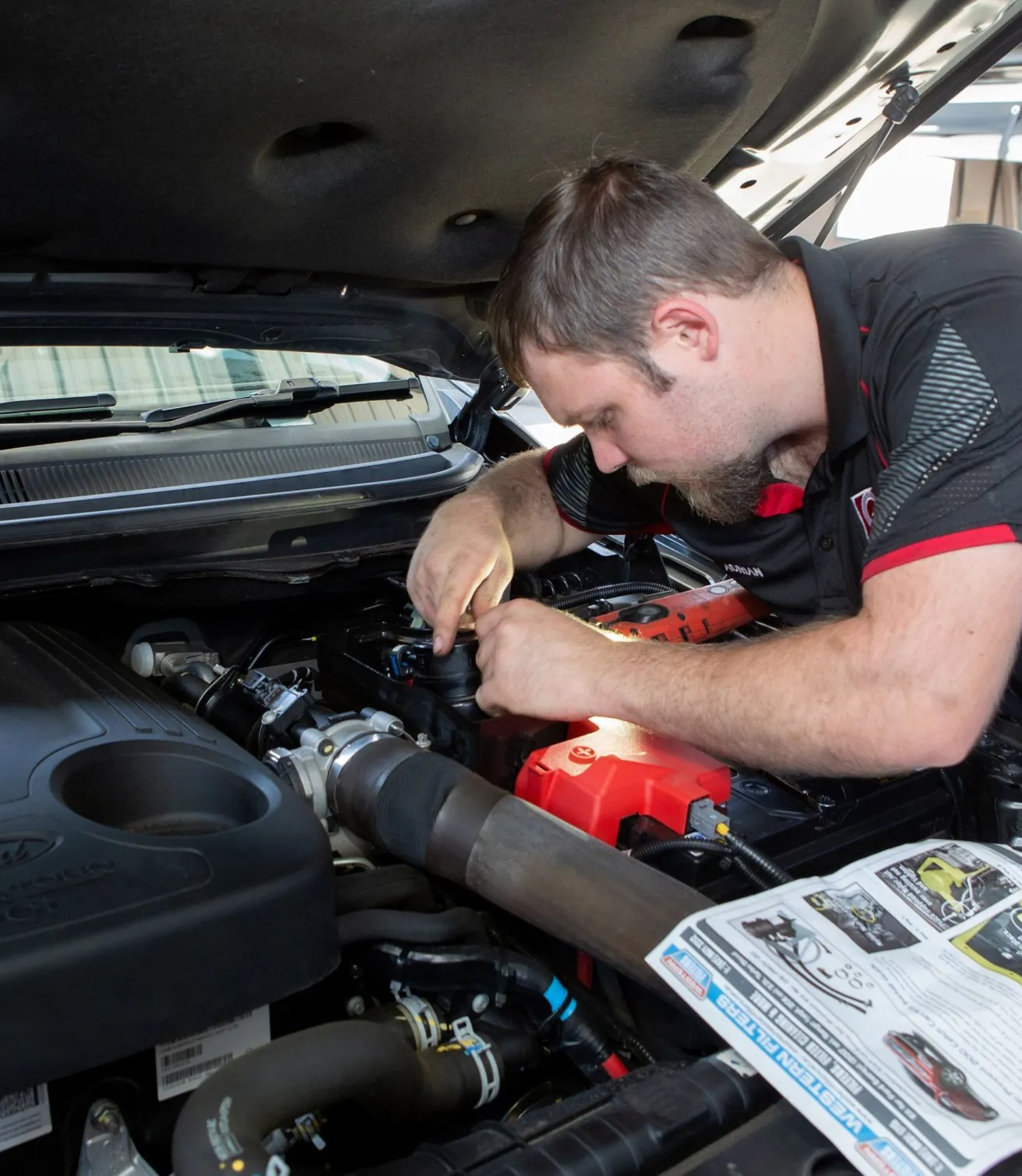 A mechanic working in an engine bay with the service manual open on the wing