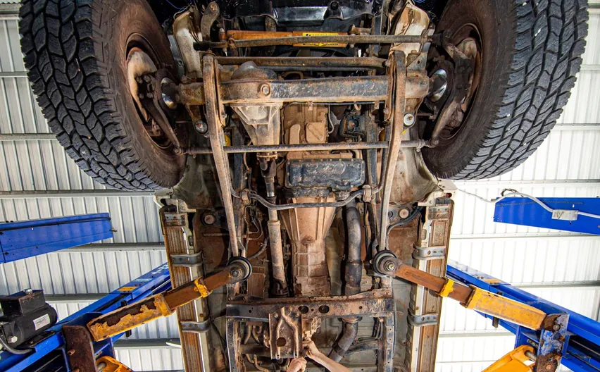 Looking up at the chassis and suspension of a lifted 4WD on a hoist, a mechanic working underneath