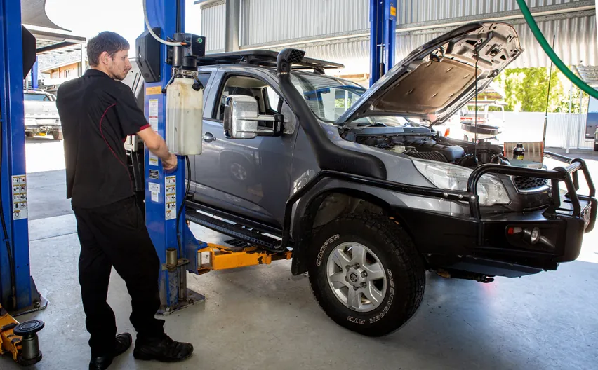 A mechanic beside a grey 4WD ute with a snorkel and bull bar, bonnet up on the hoist
